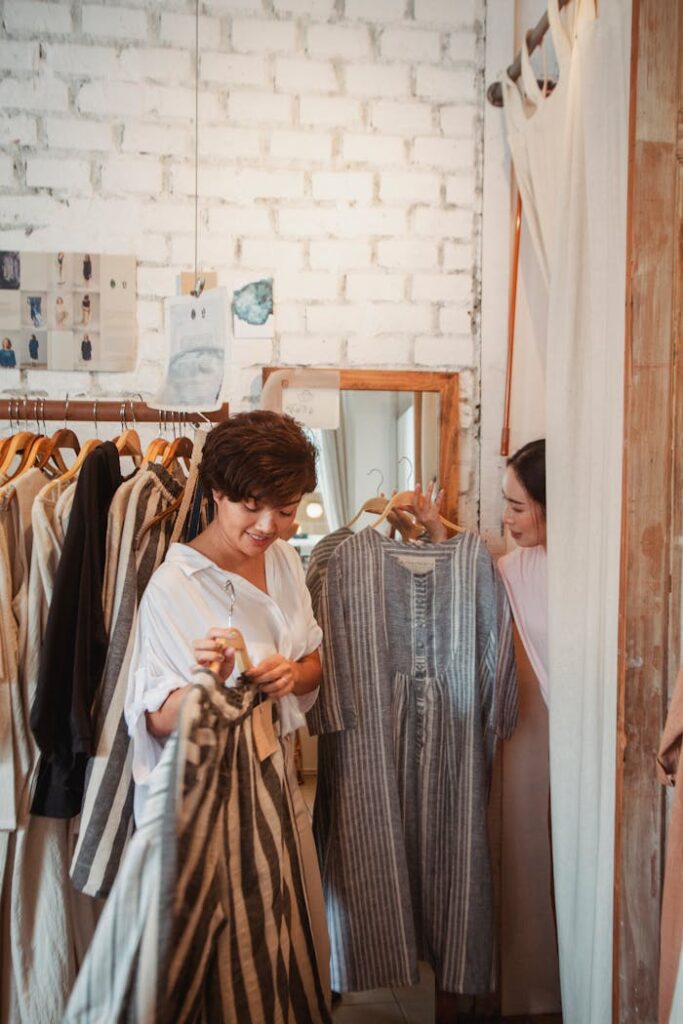 Two young women selecting stylish outfits in a cozy boutique with a cheerful atmosphere.